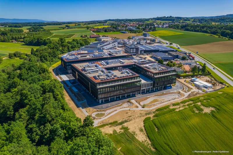 Buildings in the countryside, large windows, solar panels on the roofs, trees, construction site
