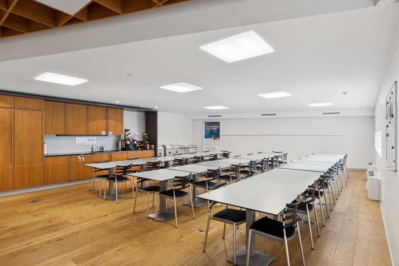 empty room with white tables and chairs, wooden floor, wooden cabinets, white walls, posters, ceiling lights