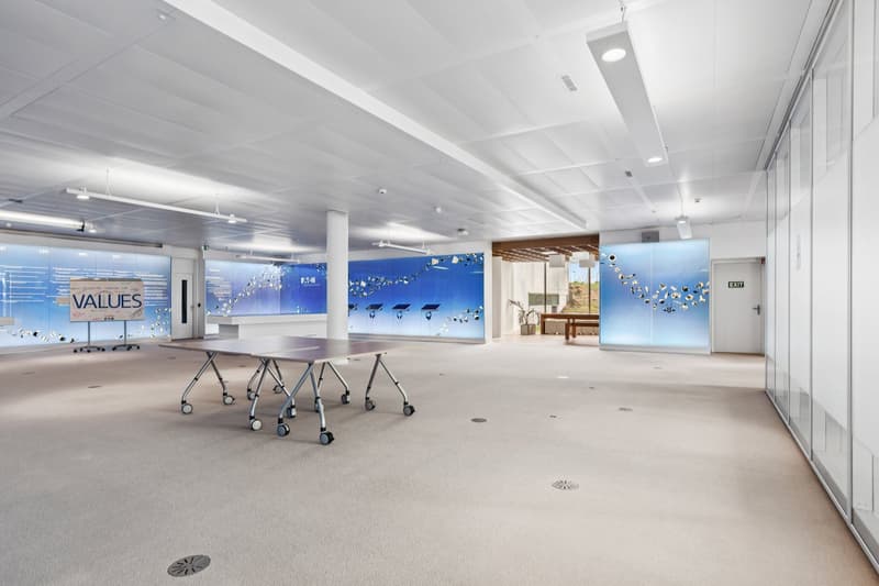 large open space, white walls, blue wall graphics, movable tables, carpeted floor, ceiling lights