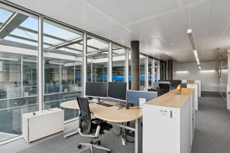 modern office space with large windows, glass walls, desks, computer monitors, office chairs, cabinets, and a pillar