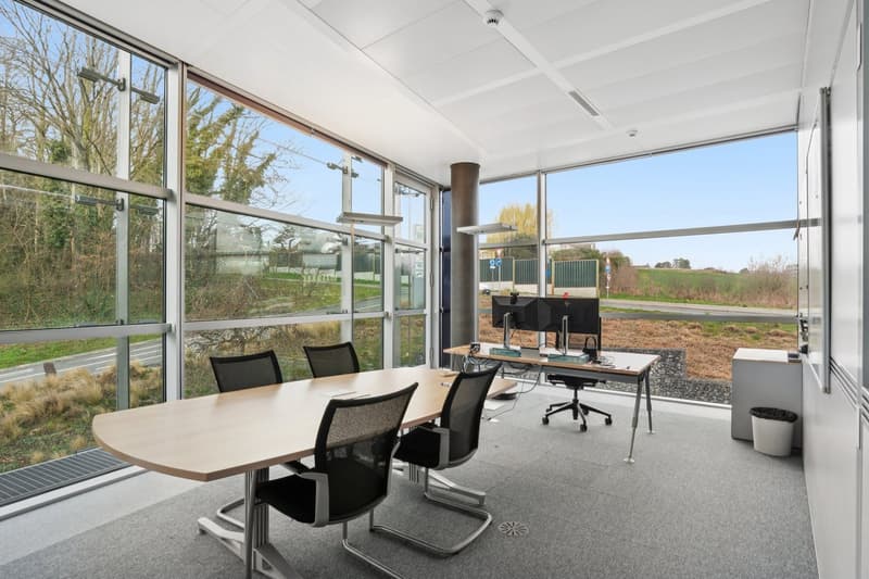 modern office room with large windows, wooden desk, black chairs, computer monitors, trash bin