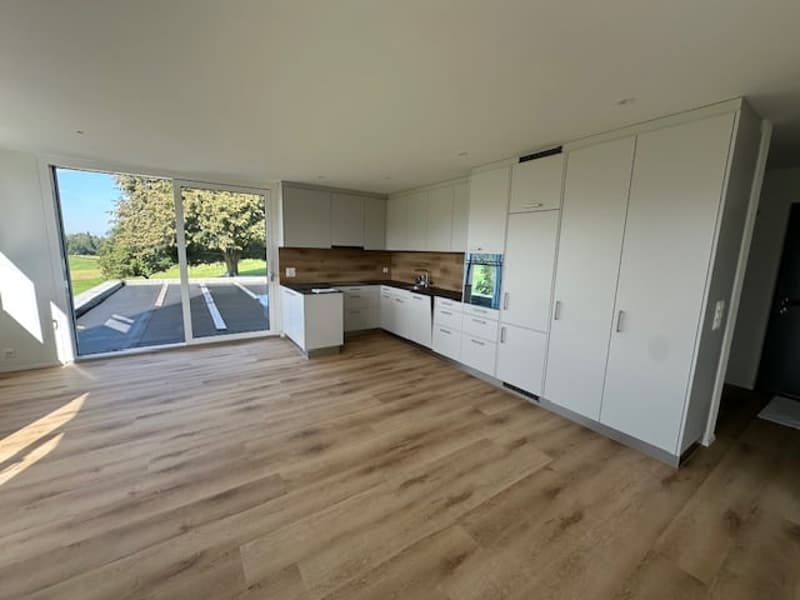 modern kitchen with wooden floor, white cabinets, large windows, and a sliding door leading to a parking area
