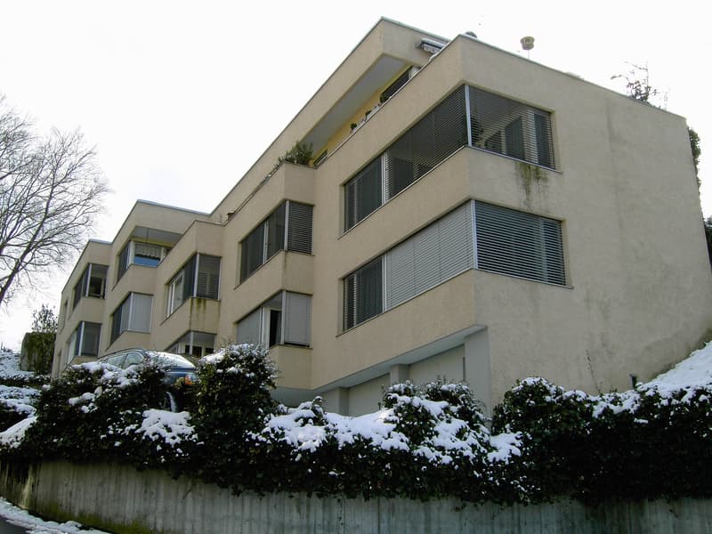 large multi-story building, cream exterior, multiple windows, small balconies, cars parked outside