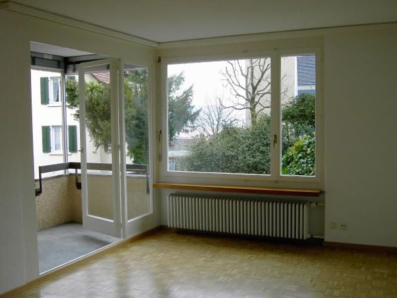 empty room with wooden floor, white walls, large windows, radiator, and sliding doors to balcony