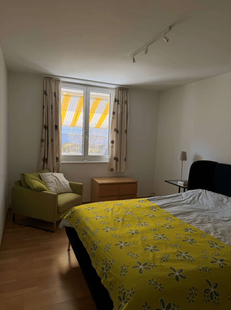 Bedroom with bed, chair, nightstand, and window with curtains