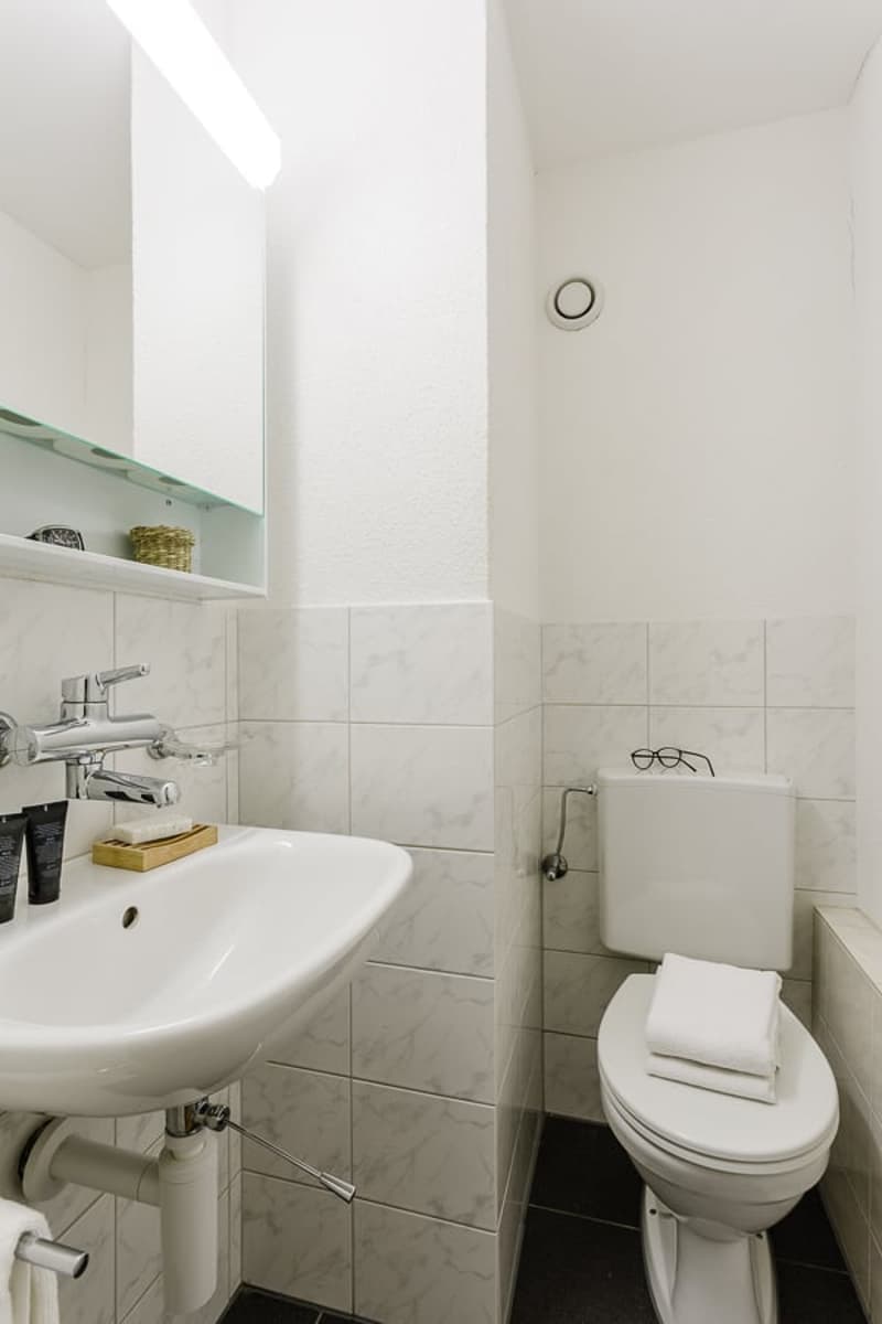 Bathroom with white tiles, pedestal sink, toilet, and shelving above the sink