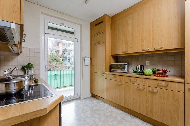 Spacious kitchen with wooden cabinets, tile backsplash, stainless steel appliances, and a sliding glass door leading to a balcony or terrace.