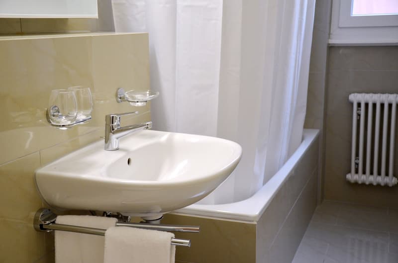 White ceramic sink with chrome faucet, glass shelves, towel rack, and radiator