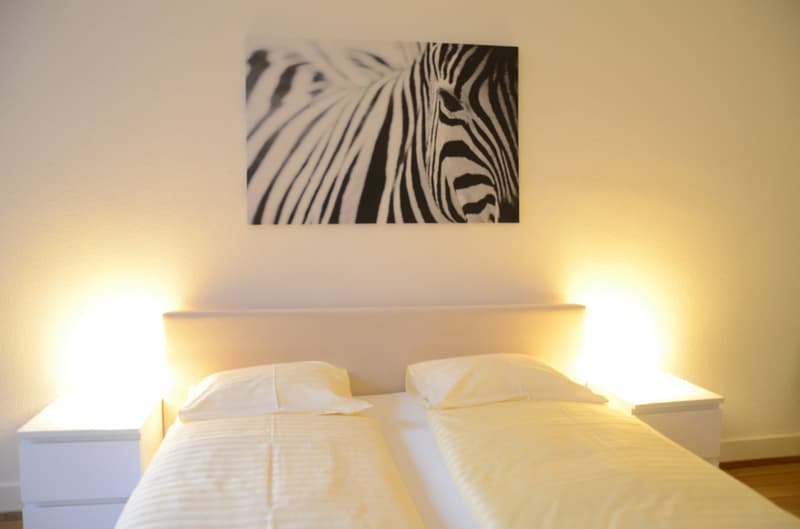 Bedroom with white bedding, white nightstands, and a large black and white zebra print artwork on the wall.