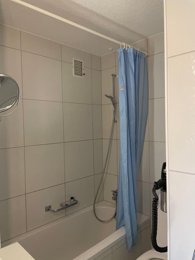 Tiled bathroom with a shower curtain, a mirror, and a washing machine visible.