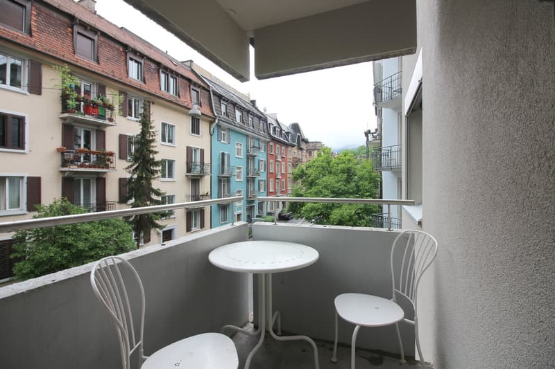 Balcony with a small table and chairs, overlooking a residential neighborhood with colorful buildings and trees