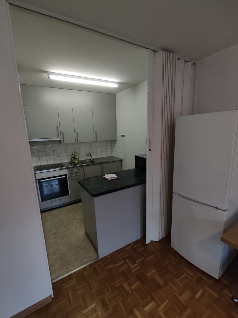 Small kitchen with white cabinets, black countertop, stove, oven, refrigerator, and tile flooring