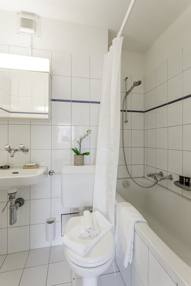 modern bathroom with bathtub, white tiles, white toilet, sink with mirror, shower curtain, potted plant
