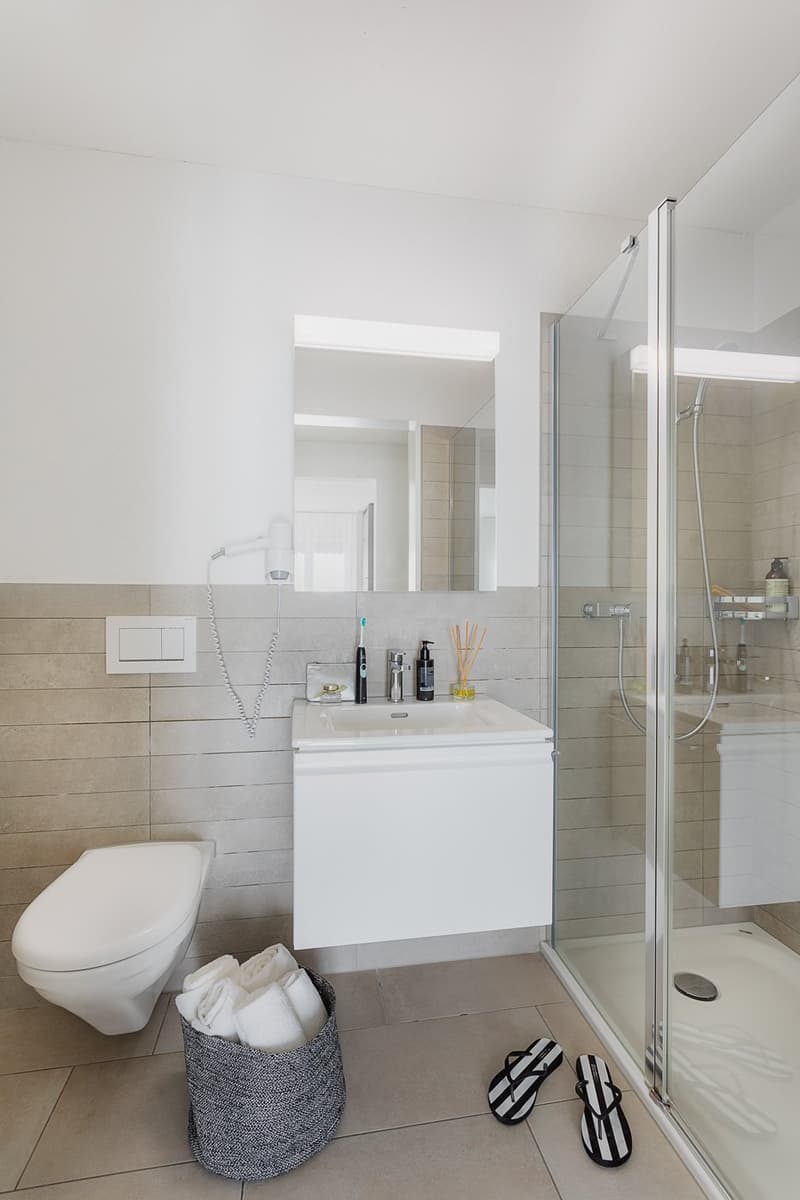 modern bathroom with walk-in shower, white toilet, vanity with sink, towels in a basket, open shower enclosure