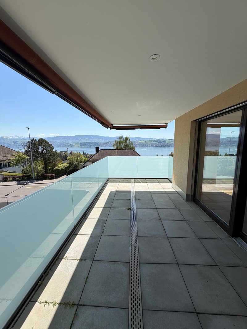Balcony with glass railing, tiled floor, view of the lake and mountains