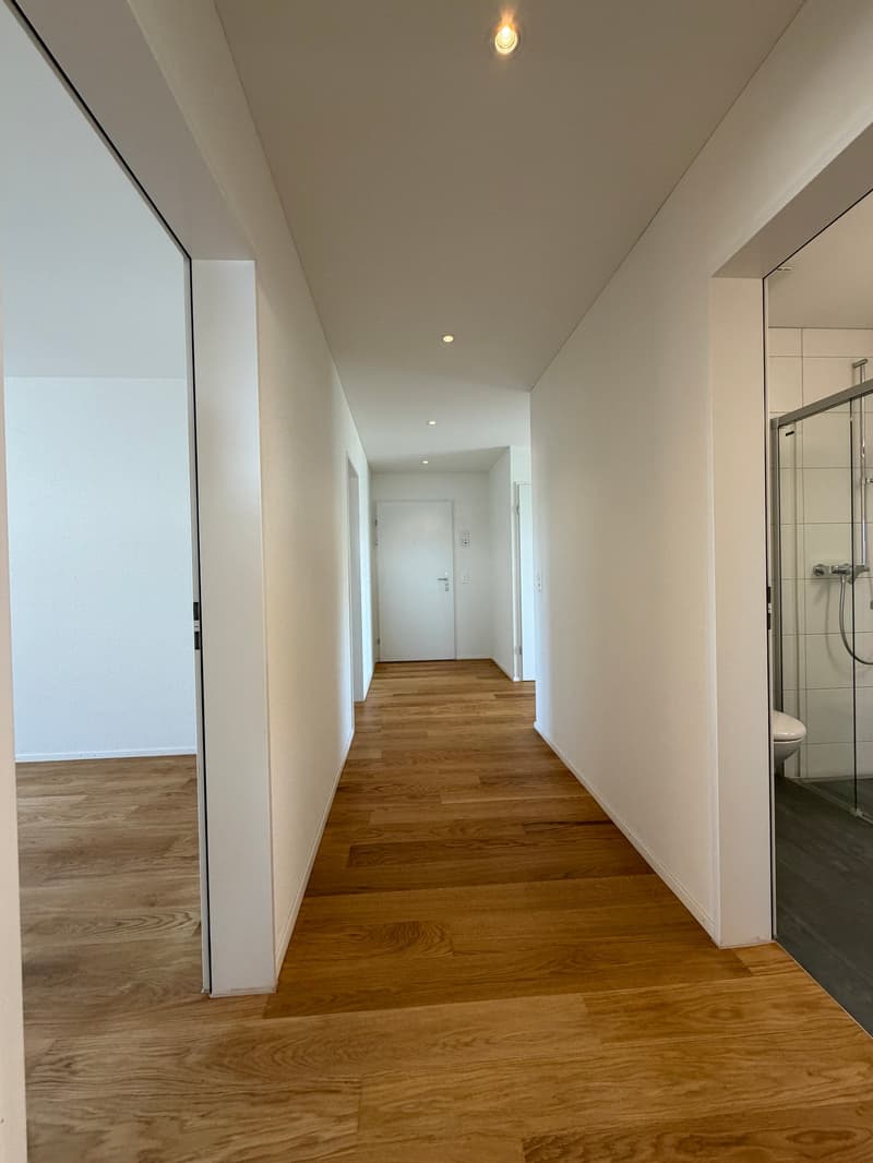 Empty hallway with wooden floors, white walls, and ceiling lights