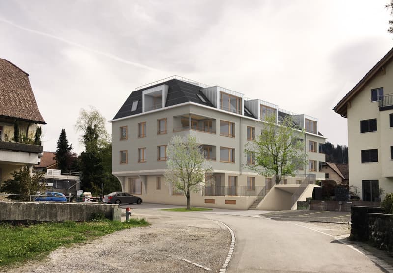 5-story modern apartment building with a mix of gray and white exterior, large windows, and balconies on some units. The building is situated in a residential area with other smaller buildings and trees around it.