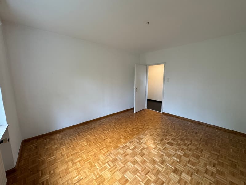 Empty room with white walls, wooden parquet floor, open door leading to another room