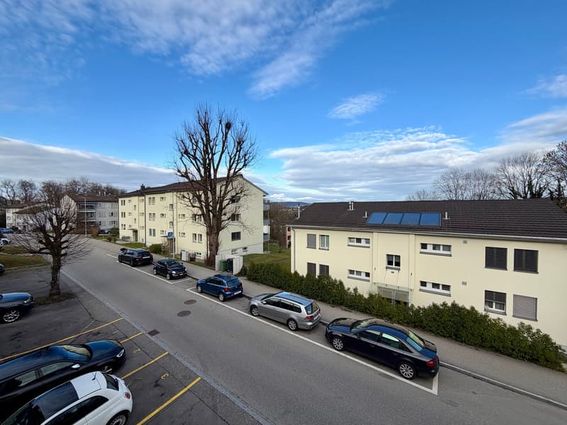 Aerial view of a street with multiple cars parked in front of a building with solar panels on the roof.