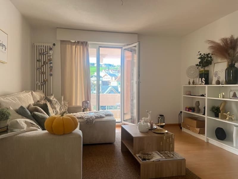 large windows, sliding glass door to balcony, beige couch, coffee table, open bookshelves