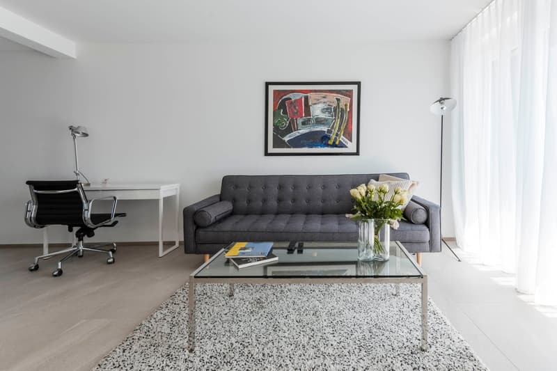 modern apartment living room with glass sofa, glass coffee table, black office chair, white desk, modern floor lamp, white floor and walls, and window drapes