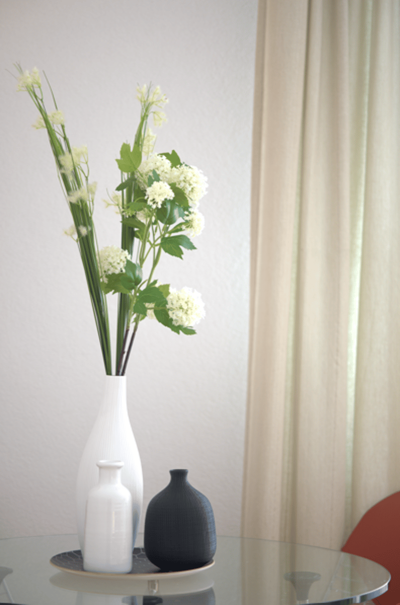 round glass table, round glass vase, white flowers, plate with a small white vase, a black vase