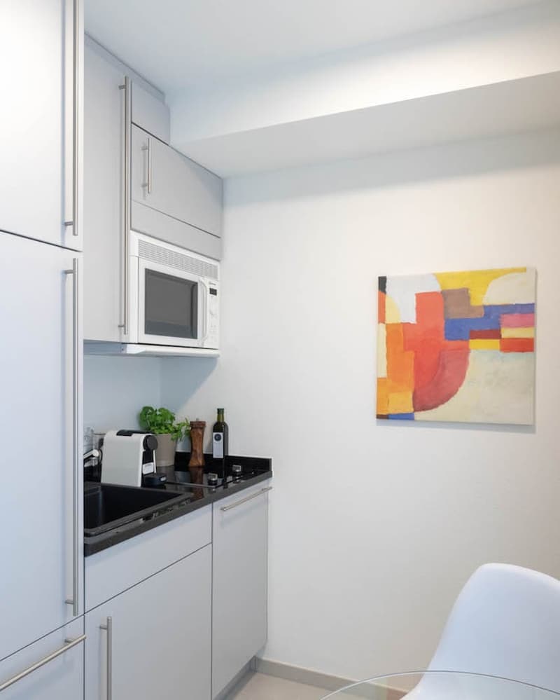 White cabinets, black countertop, microwave, sink, toaster, painting
