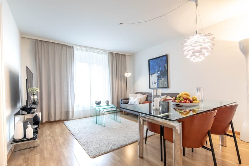 modern dining area with a glass table and wooden floor, beige rug, chairs, TV, chandelier, artwork