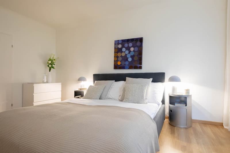 a tidy and minimalistic bedroom with a double bed, bedside tables, nightstands with lamps, and a small cabinet.