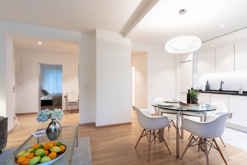Glass top table, white chairs, white walls, hardwood floor, potted plant, chandelier, glass vase, fruit bowl, white kitchen, sink, faucet