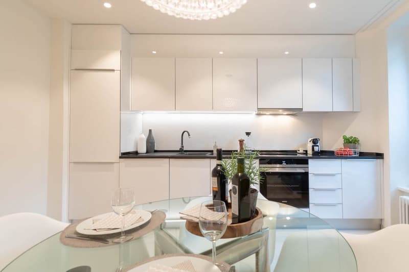 modern kitchen, white cabinets, black countertops, glass table, wine glasses, bottles, plants