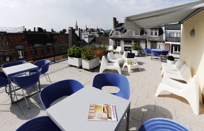 modern blue chairs, white tables, tiled floor, outdoor plants, city view, shaded seating area