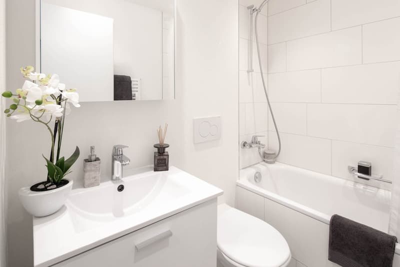 modern bathroom with white tiles, white sink, white bathtub, white toilet, white mirror, white flower vase, white towel