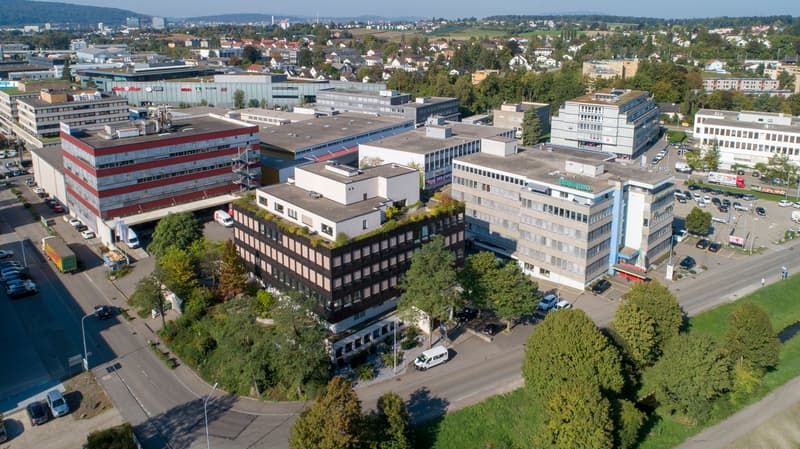 Aerial view of a commercial building complex with multiple buildings, parking areas, and surrounding greenery.