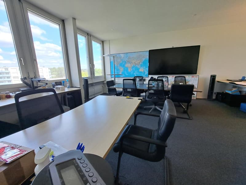 Office room with large windows, desks, chairs, a table, a television, a map, and a printer.