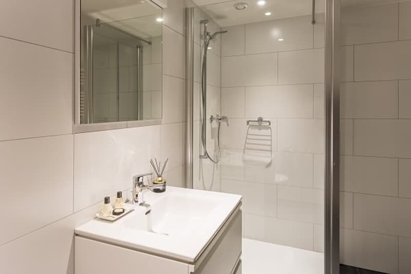 Modern bathroom with white tiles, vanity with sink, mirror, and a glass-enclosed shower area