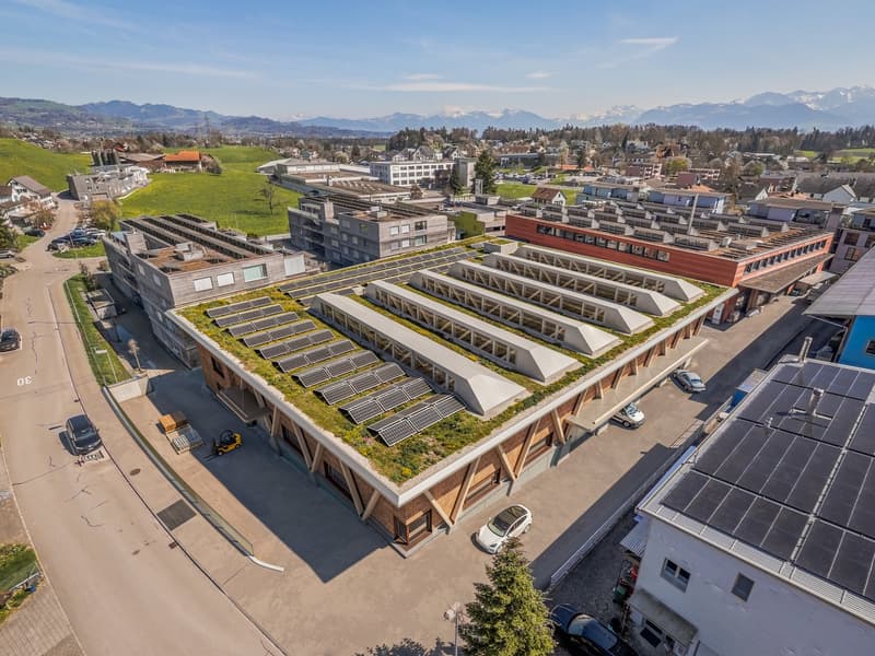 Building with solar panels on the roof, situated in a scenic location with greenery and mountains in the background