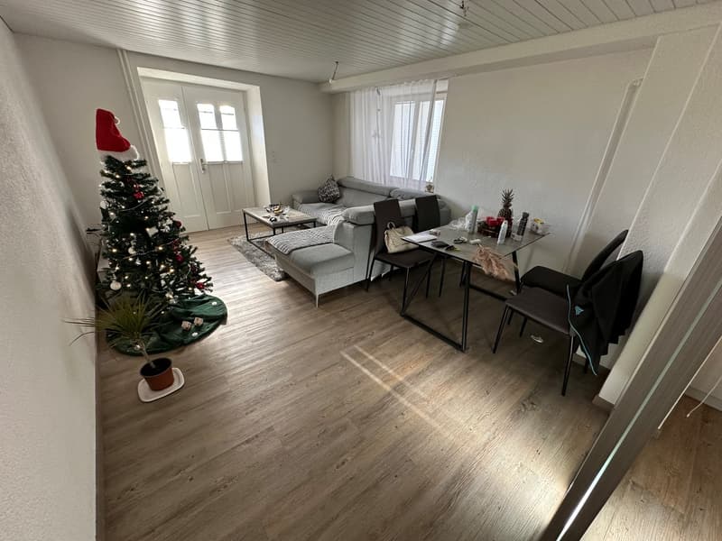 living room with wooden floor, white walls, grey sofa, coffee table, dining table, 2 chairs, Christmas tree, potted plant, rug, side table, windows with curtains