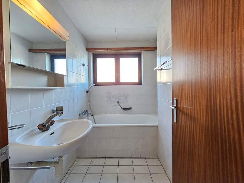 Tiled floor, white bathtub, vanity with sink, mirror, window with wooden frame