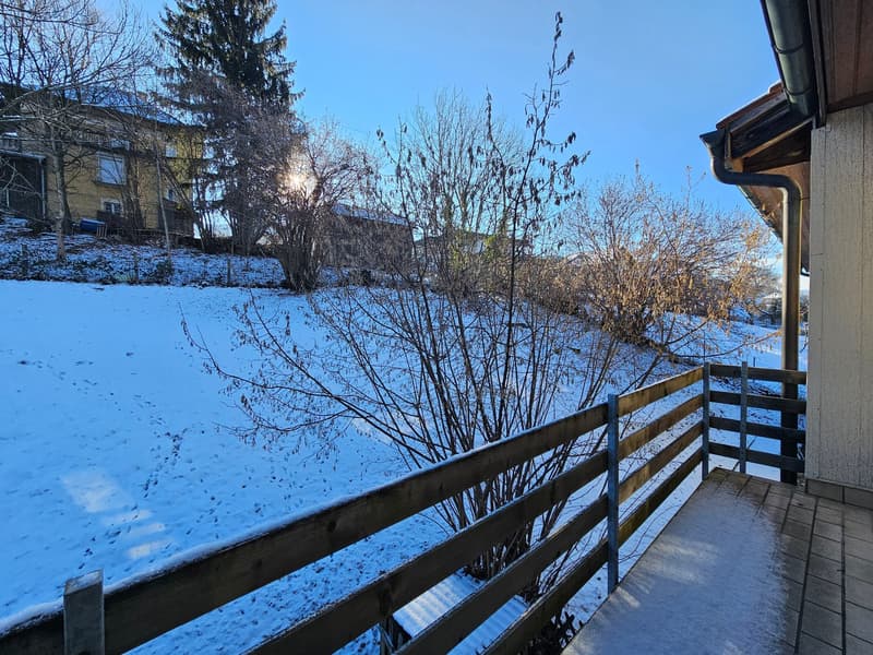 wooden railing on balcony, snowy field, blue sky, building in background