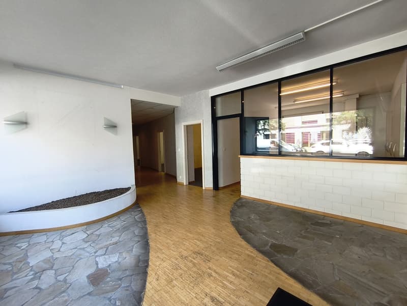 Large open space with stone walls, hardwood floors, and a fireplace. There is a reception area with a counter and glass windows overlooking the street.