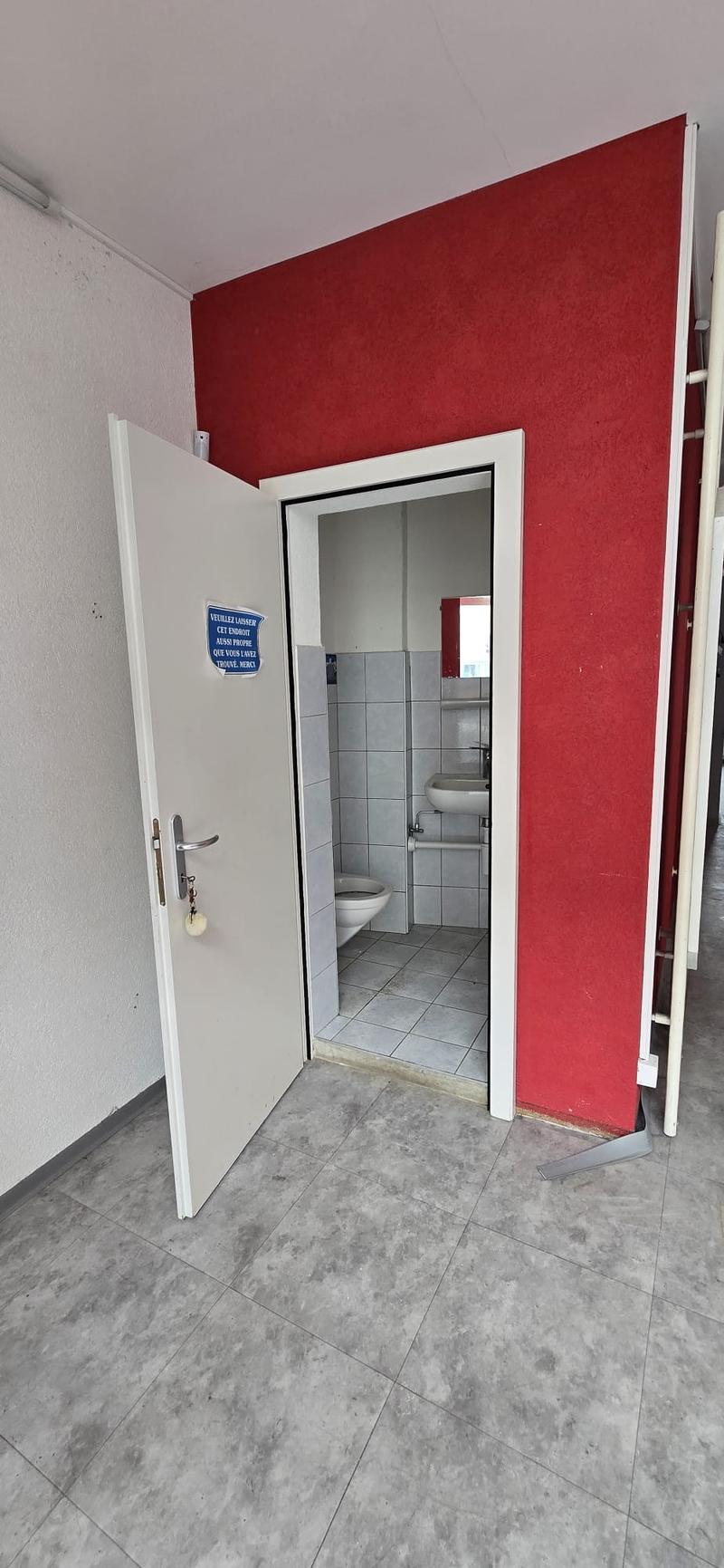 Bathroom: white tiled floor, red wall, small toilet, white sink, mirror, door