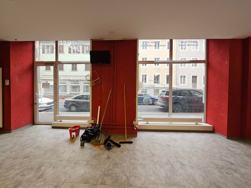 empty room with red walls, tiled floor, 3 large windows, equipment and cleaning products scattered on the floor