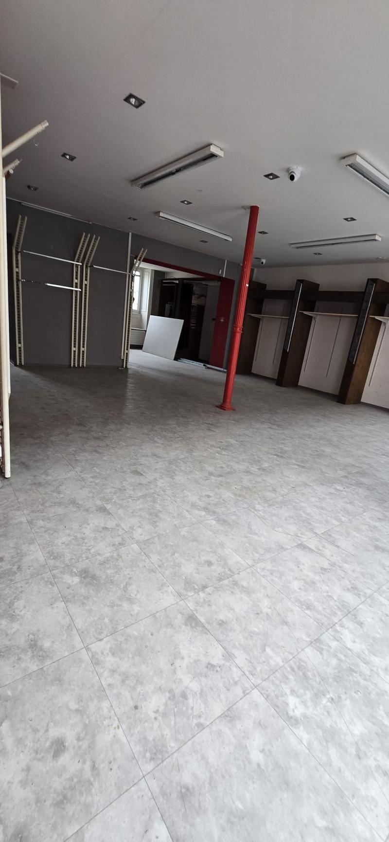 Empty room with tiled floor, ceiling lamps, metal storage racks on left wall, security cameras installed on ceiling