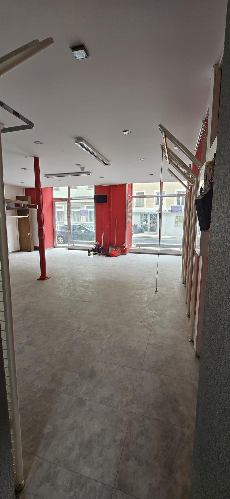 an empty room with red walls, a concrete floor, ceiling lights, a red pillar, and glass windows with a view outside.