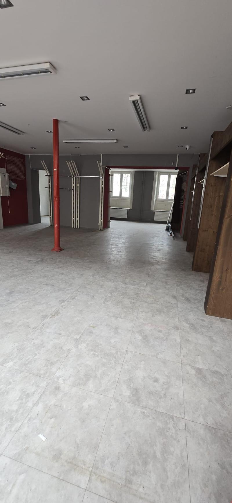 empty room with white tile floor, grey walls, a red column in the center, two entrance doors on the right, windows in the back