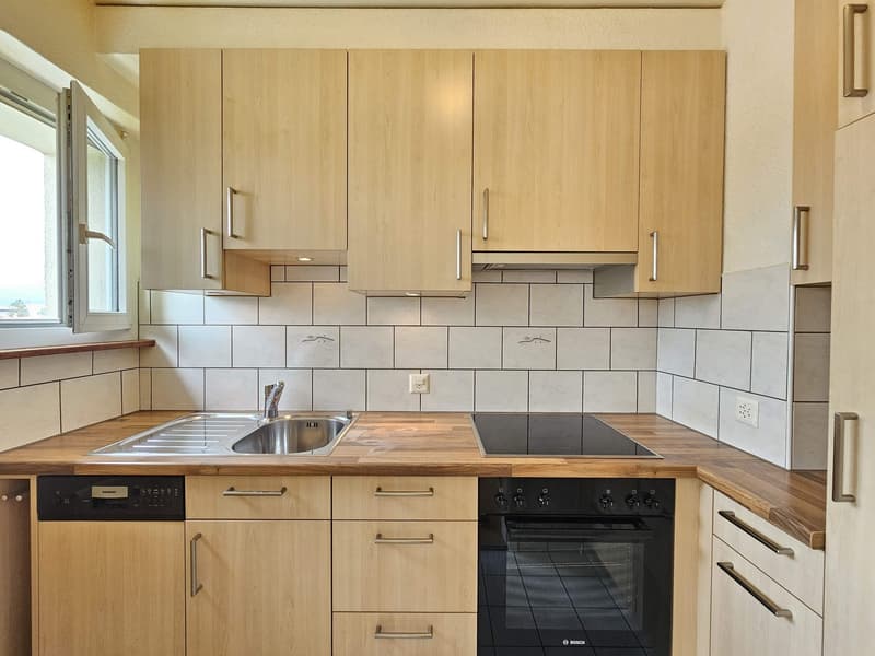 Spacious kitchen with light wood cabinets, tile backsplash, stainless steel sink, and built-in dishwasher and oven