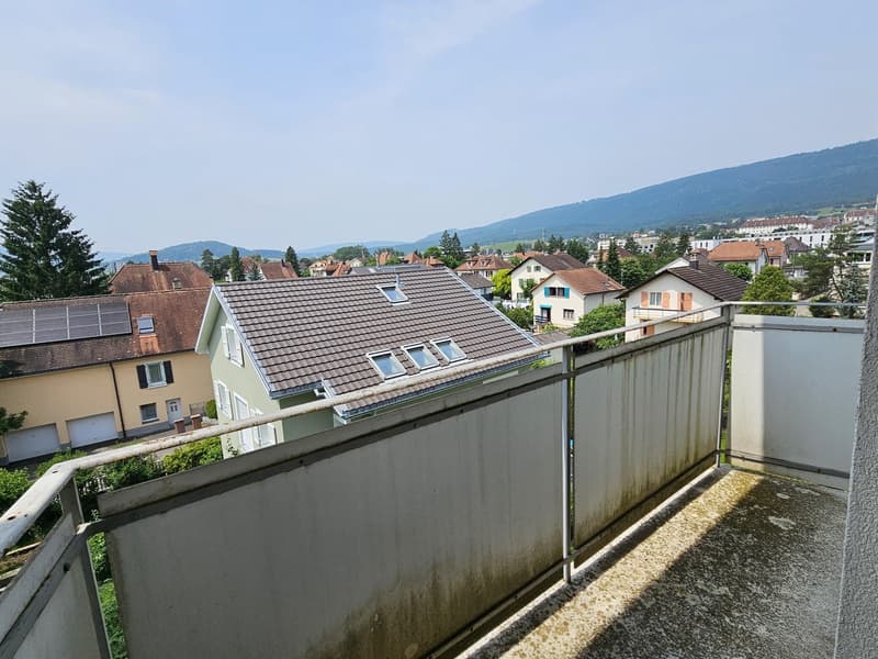 The image shows a residential building with a balcony or terrace visible. The building has a tiled roof and appears to be surrounded by other residential buildings in a hilly, mountainous area.
