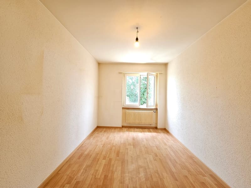 empty room with wooden floor, white walls, single window, heater
