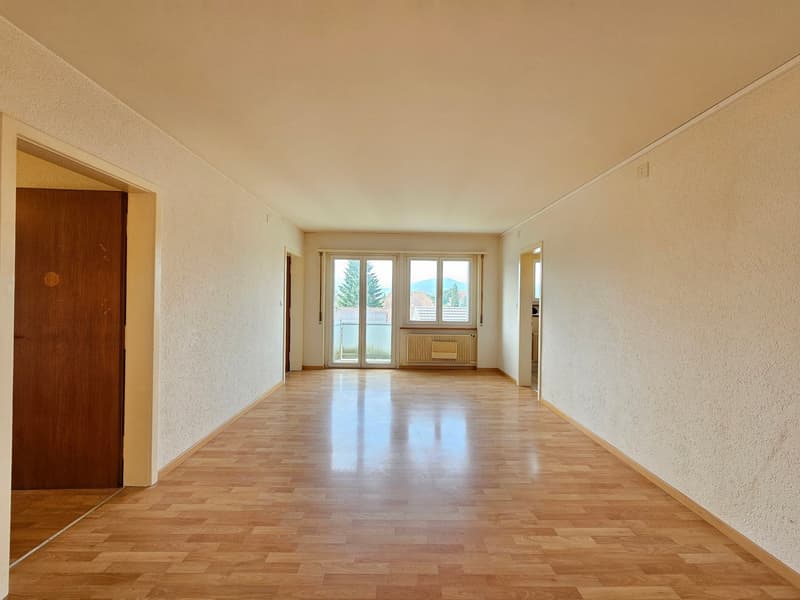 large empty room, wooden floor, sliding doors to balcony, windows with mountain view